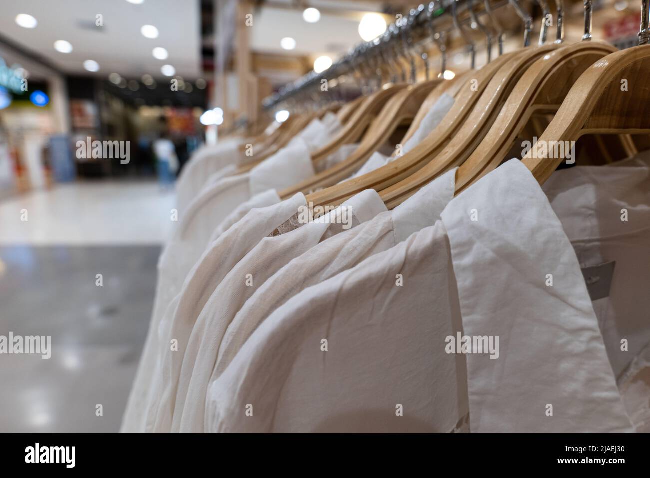 White clothes hanging on wood racks. Clothing for women hanging on hangers in shopping mall for sale. Stock Photo