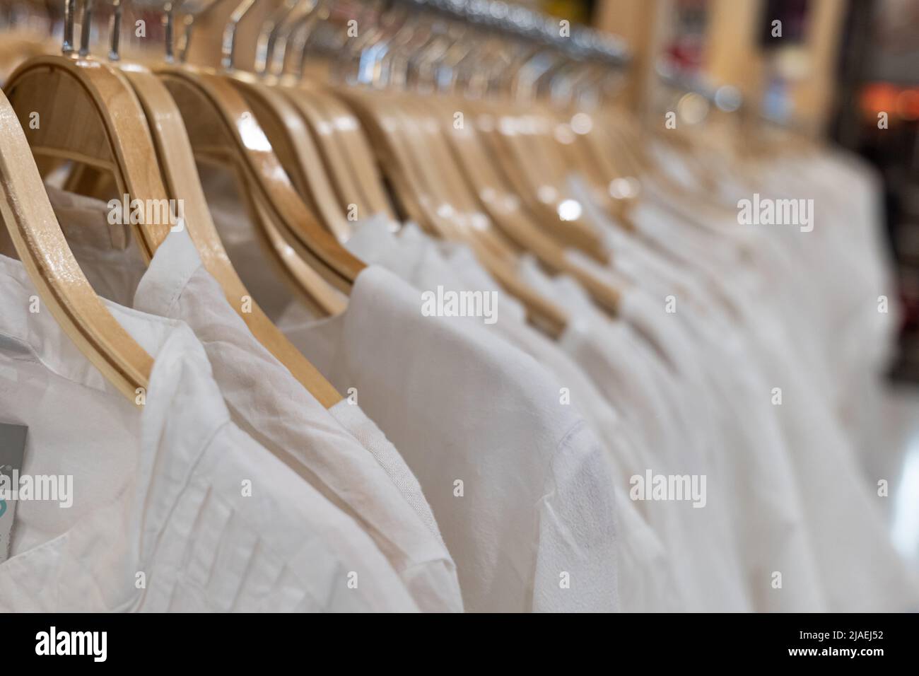 White clothes hanging on wood racks. Clothing for women hanging on hangers in shopping mall for sale. Stock Photo