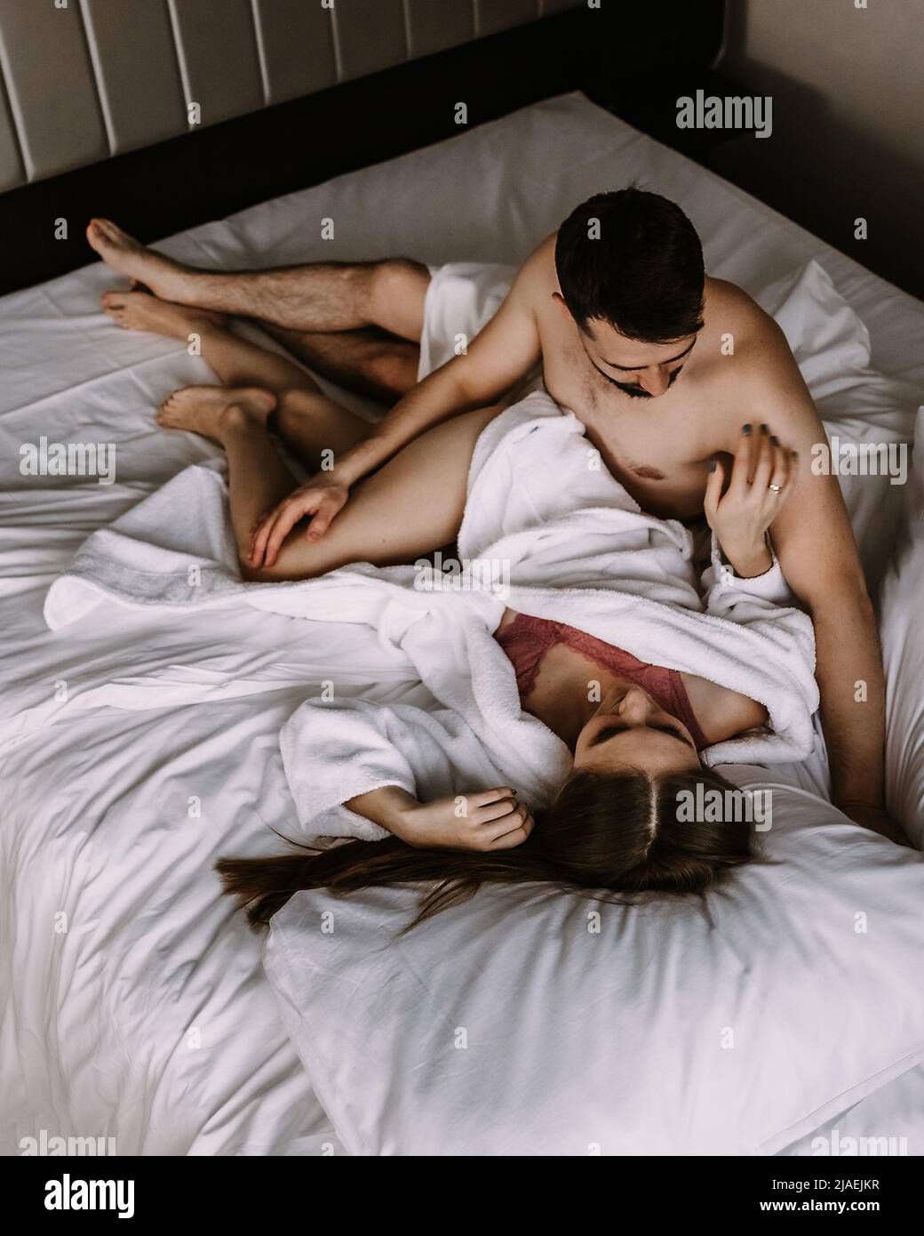 Top view of young couple in love in bathrobes lying in bed and cuddling Stock Photo