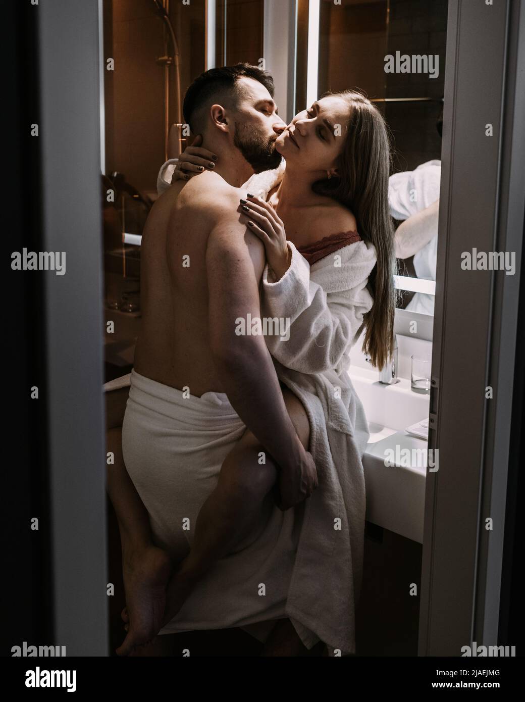 Romantic couple cuddles and kisses at mirror in bathroom Stock Photo