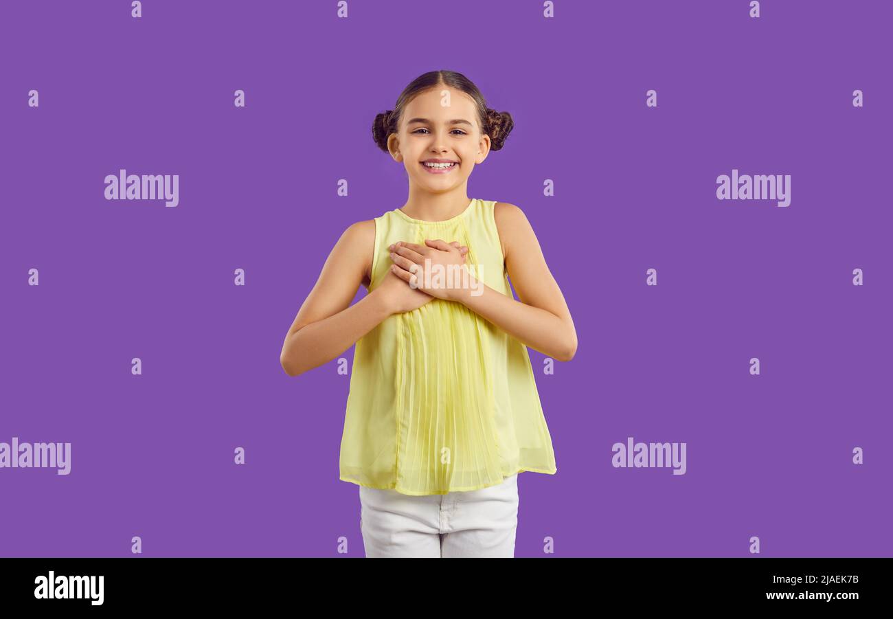 Positive happy grateful preteen girl holding hands on chest isolated on purple background. Stock Photo