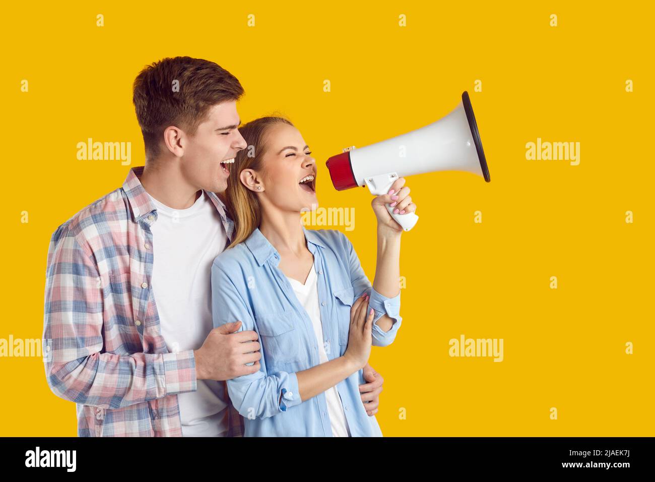Funny joyful young couple with loudspeaker making loud advertisement on orange background. Stock Photo