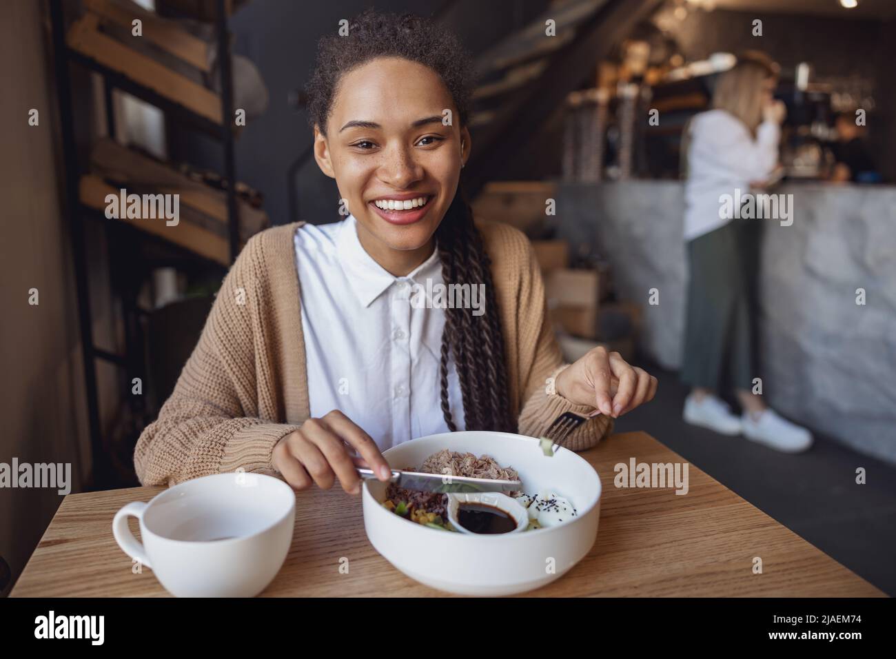 Portrait of cheerful African young woman smiling toothy smile to camera while snacking at a food and drink establishment Stock Photo