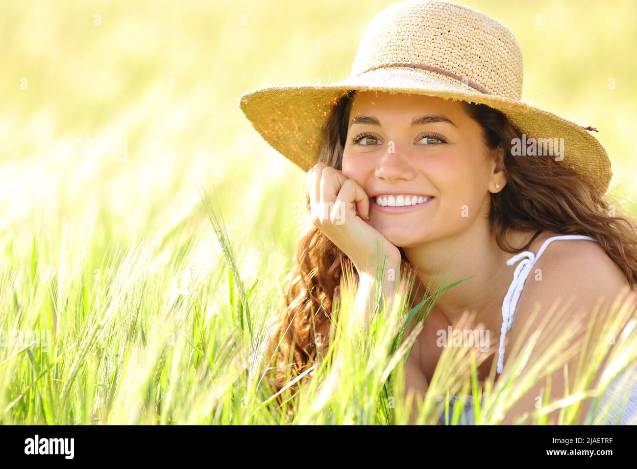 Portrait of a happy woman with white smile sitting in a wheat field looking at camera Stock Photo
