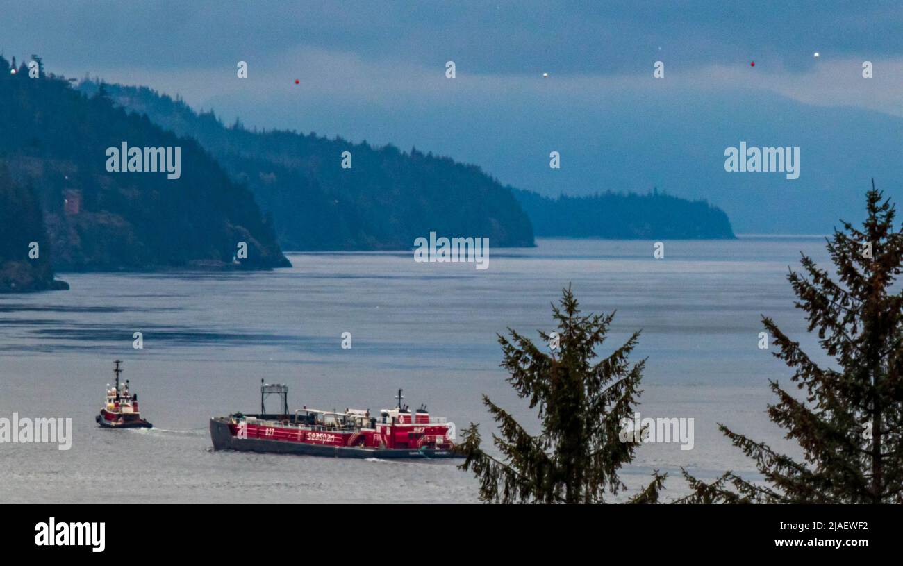 A tug pulls a loaded barge through Seymour Narrows, Discovery Passage, between Vancouver island and the Discovery islands.  Blue tone, coastline. Stock Photo