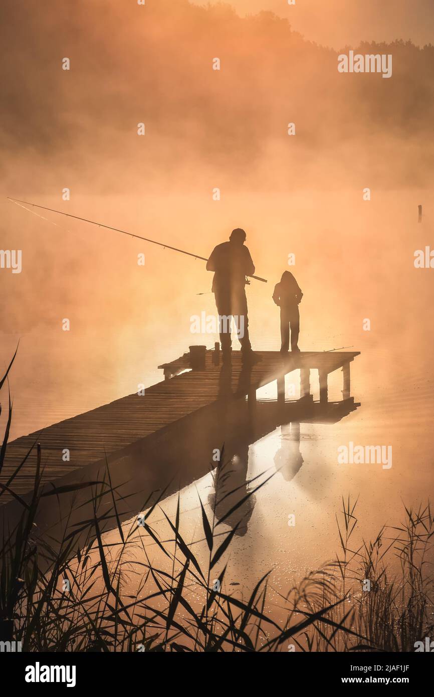 Beautiful morning scene by the lake. Father and son fishing in the light of the rising sun. Stock Photo