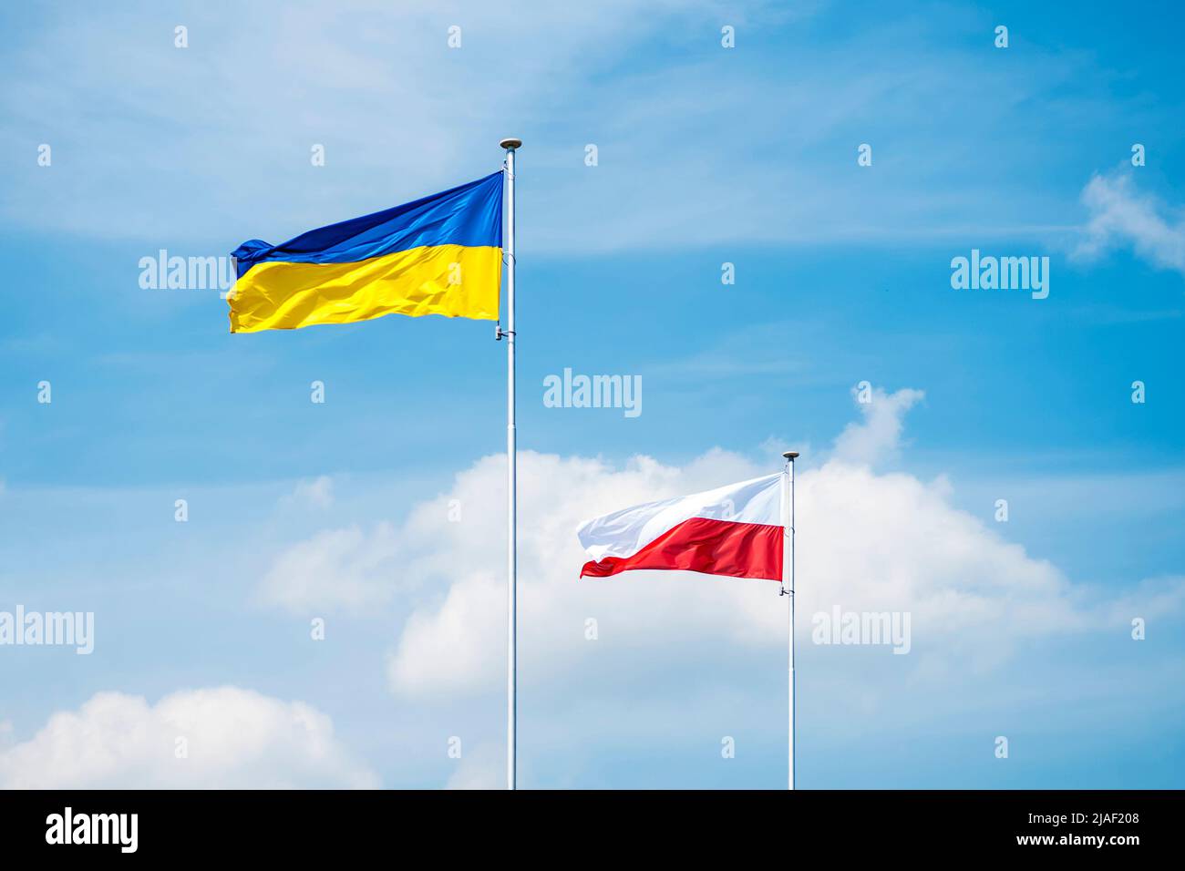 State flags of Ukraine and Poland on flagpoles over blue cloudy sky background. Stock Photo
