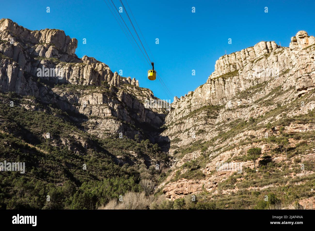 Yellow Cableway to Montserrat Mountain in Catalonia during Sunny Summer Day. Rocky Hill in National Park in Spain near Barcelona. Stock Photo