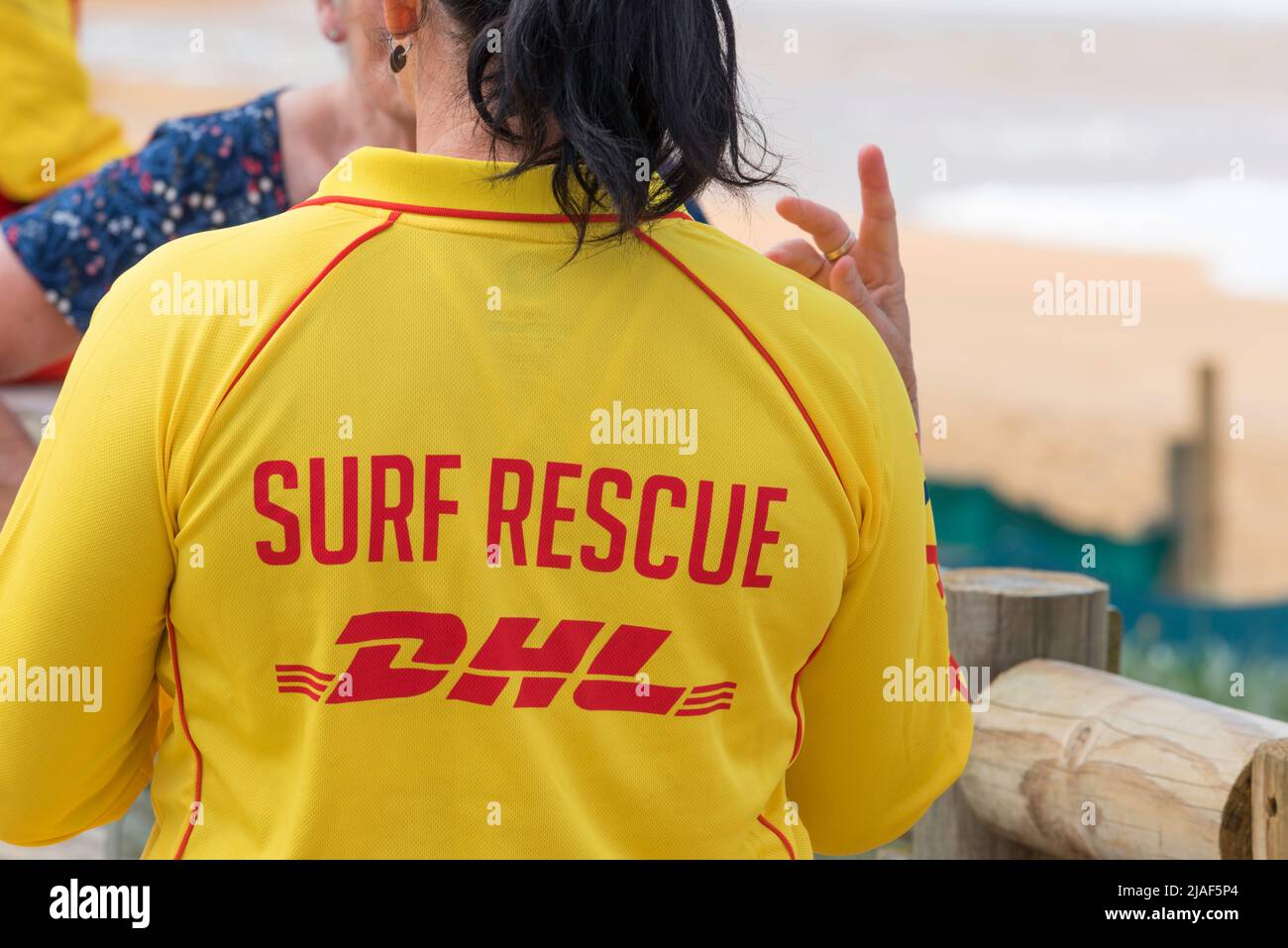 A woman wearing a distinctive Surf Life Saving Australia yellow top speaks to someone  at a beach in New South Wales, Australia Stock Photo