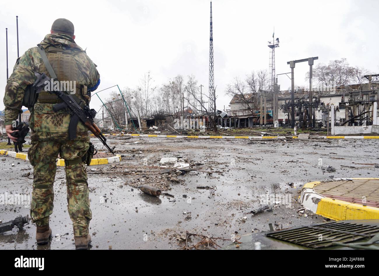 A military man with a machine gun stands against the backdrop of a devastated area. During the war in Ukraine Stock Photo