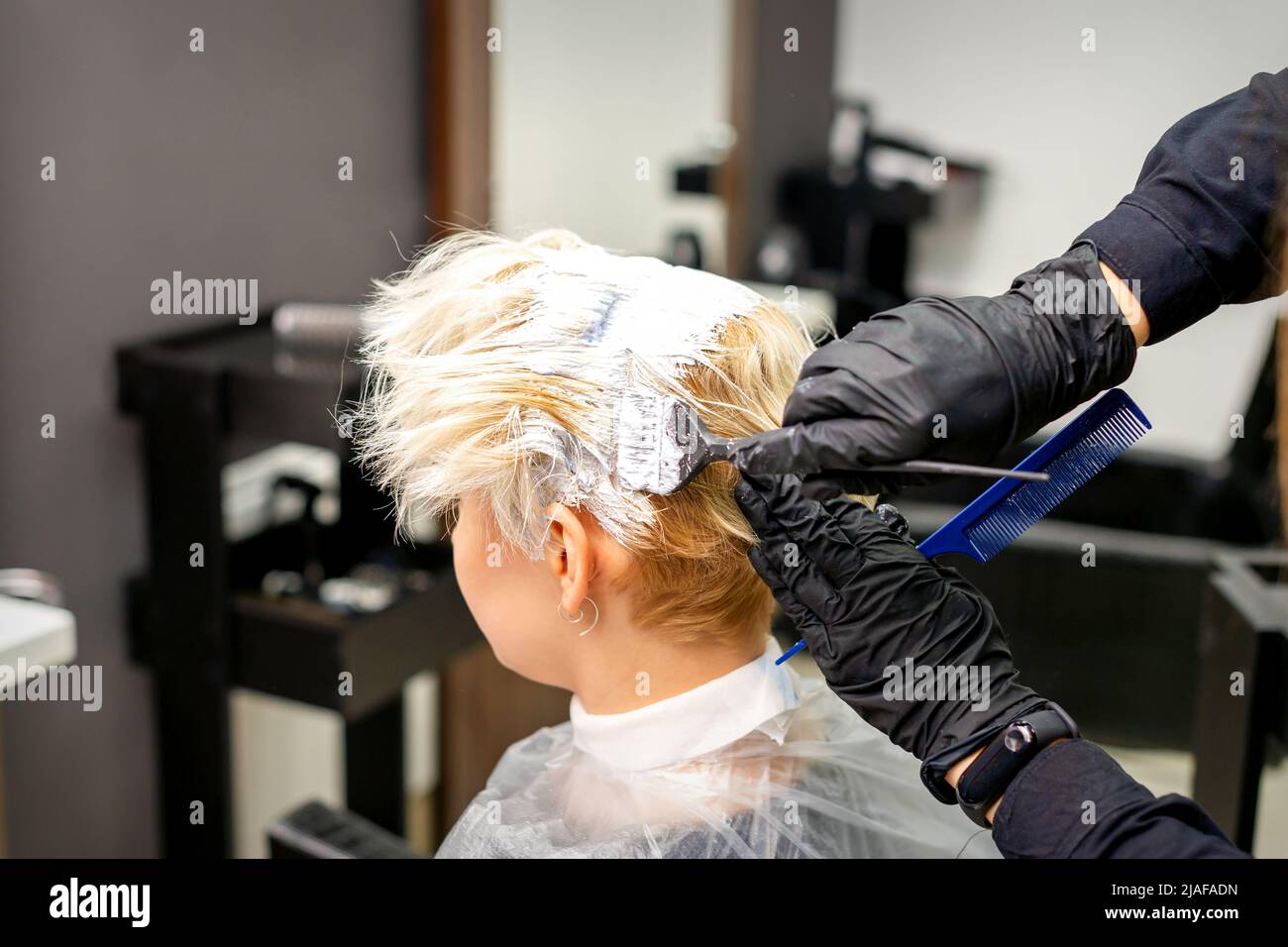 Coloring white hair with hair dye and brush by hands of hairstylist for