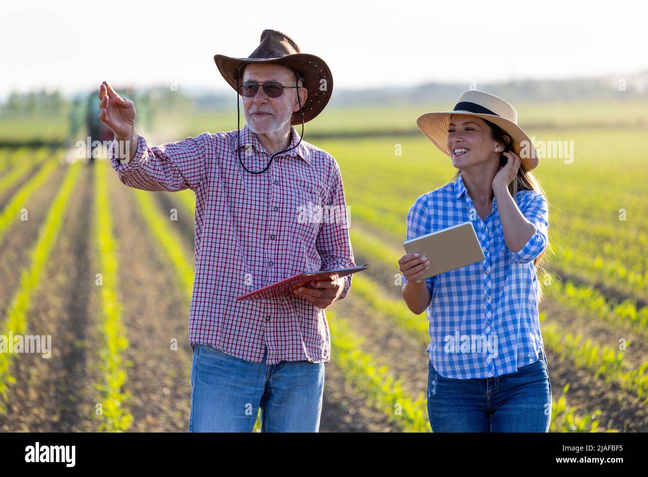 Two farmers young woman and senior man talking in soybean field in spring time at sunset Stock Photo