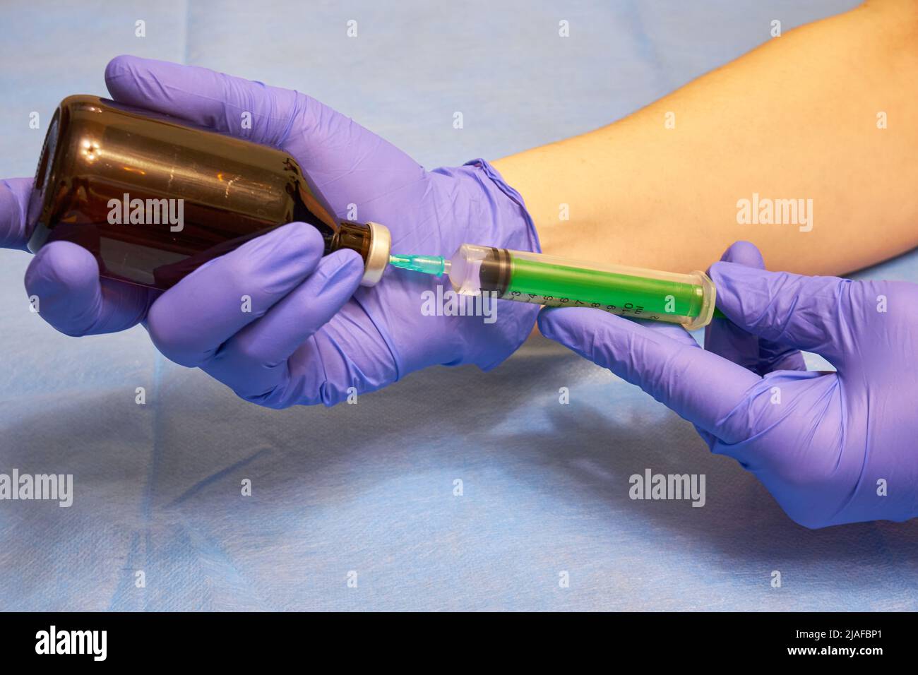 Hands in medical gloves draw liquid into a syringe from a vial Stock