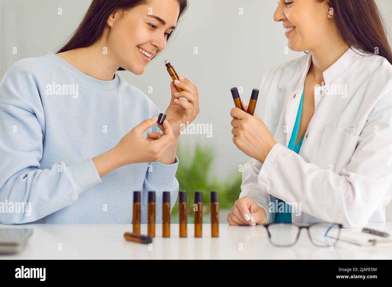 Joyful young woman chooses scent of essential oil when visiting female homeopathic doctor. Stock Photo