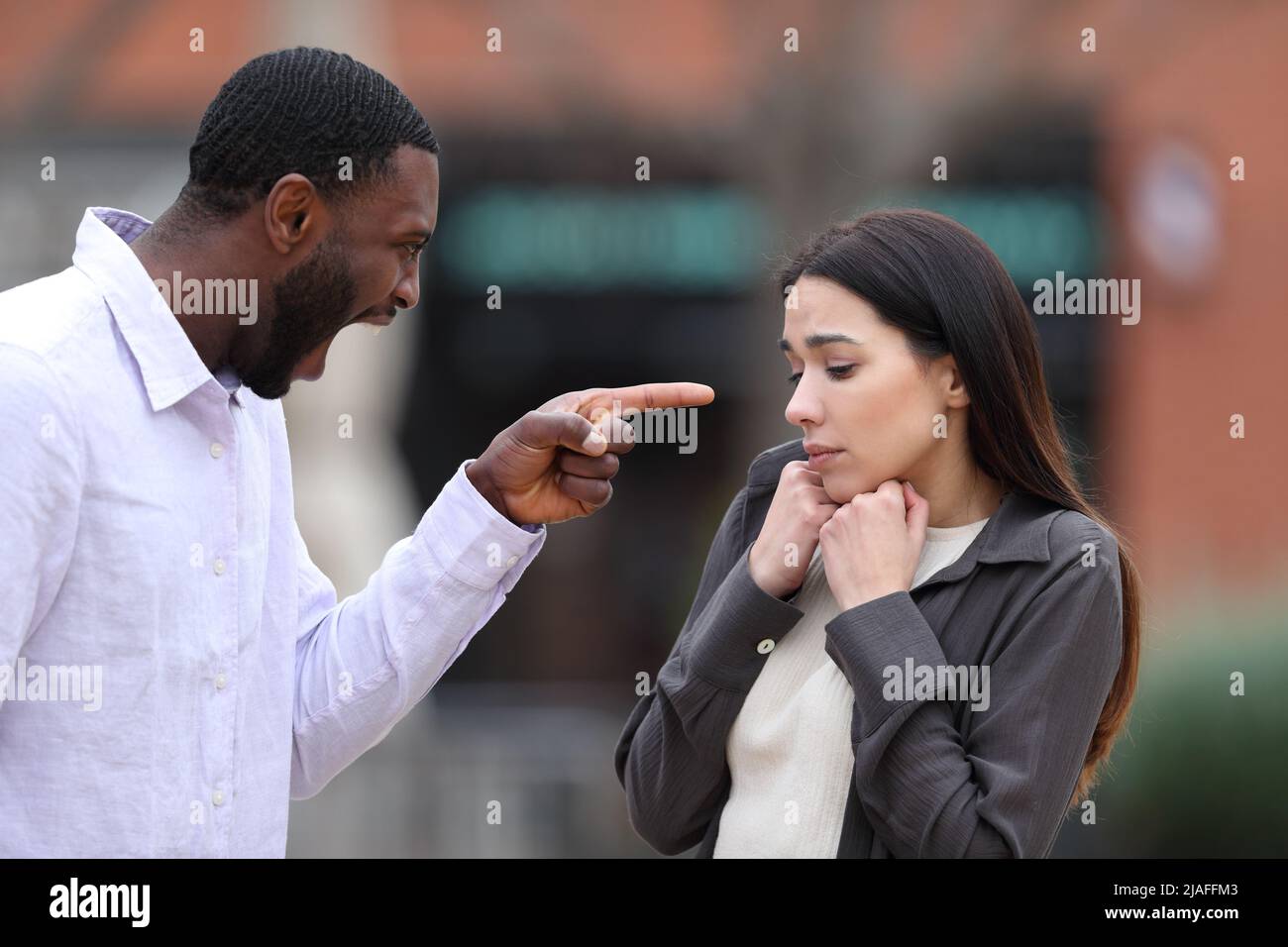Angry man scolding and accusing to a scared woman in the street Stock Photo
