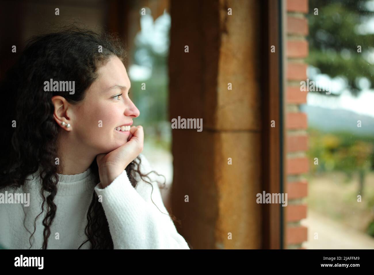 Side view portrait of a happy woman sitting looking through a window Stock Photo