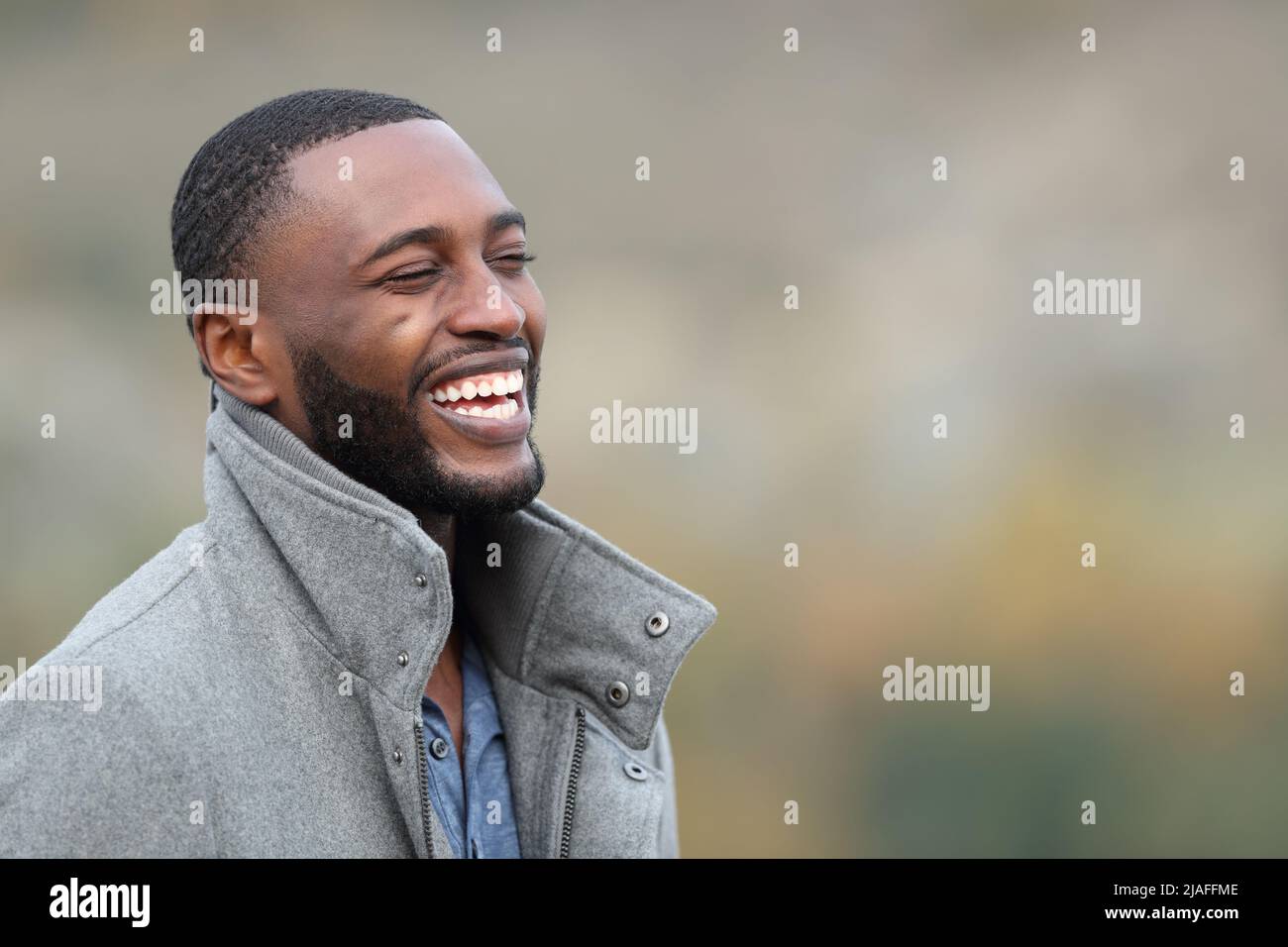 Happy man with black skin laughing in the mountain wearing jacket in winter Stock Photo