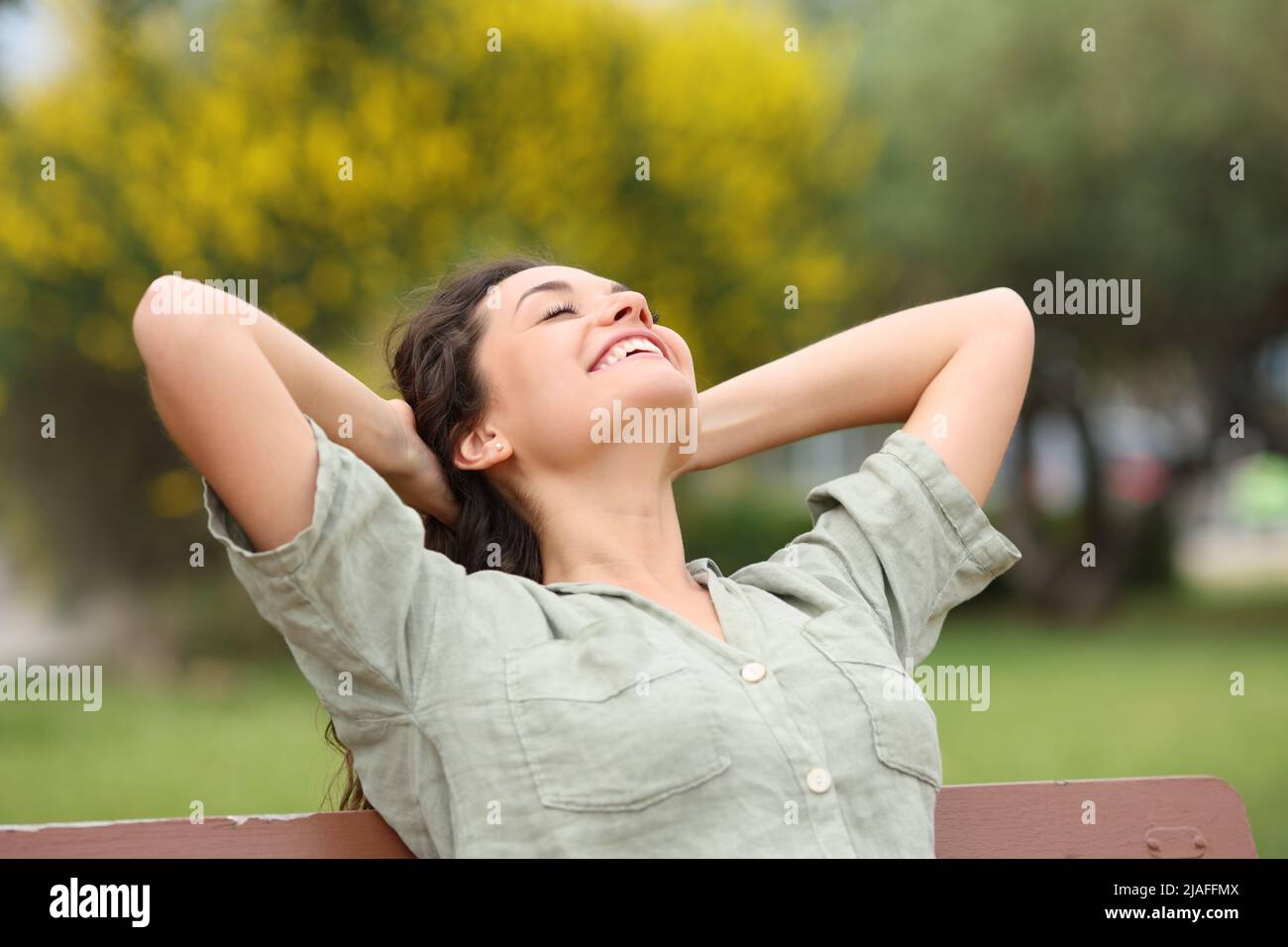 Happy woman relaxing in a park smililing sitting on a bench Stock Photo