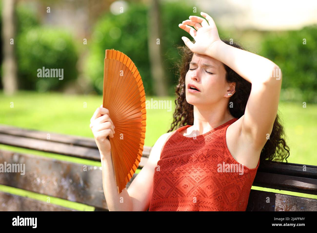 Woman in a park suffering heat stroke fanning Stock Photo