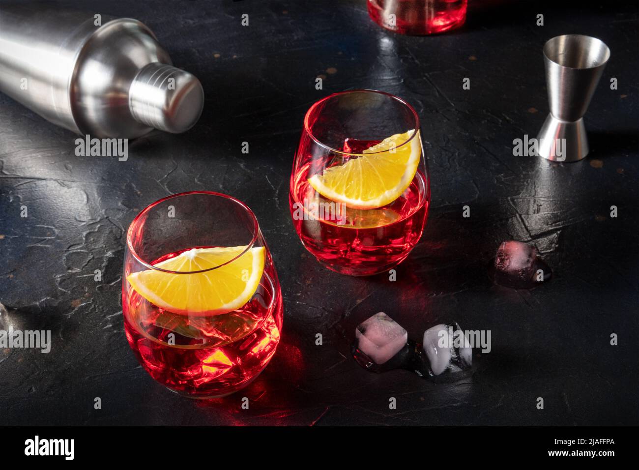Campari orange cocktails with a jigger and a shaker, with ice cubes and a bottle in the background, on a dark slate background Stock Photo
