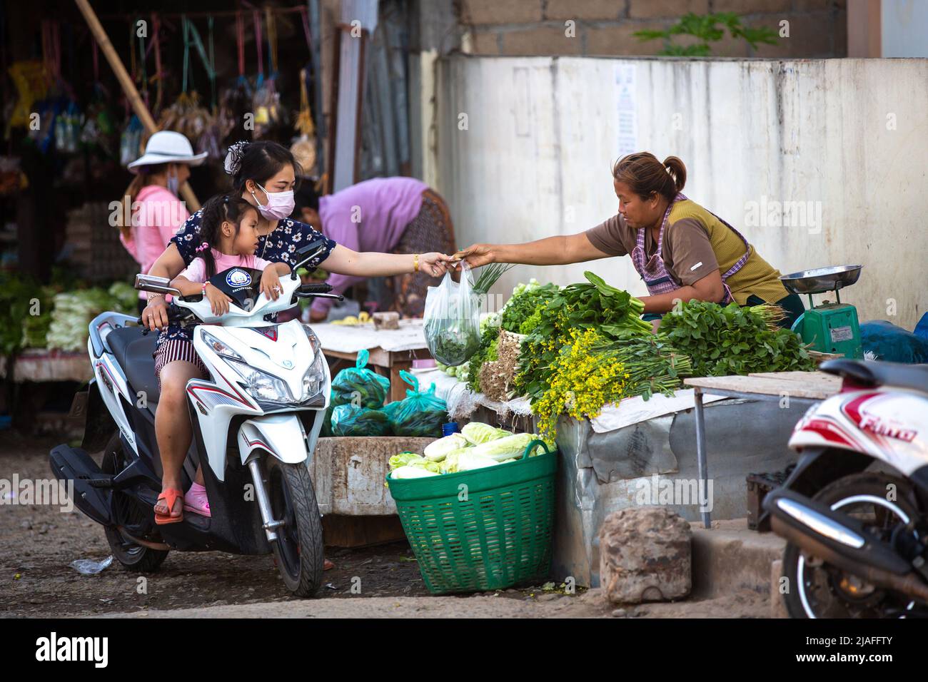 Luang Prabang, Laos - November 15, 2017: An unidentified woman wearing a face mask buying vegetables from a street seller in Luang Prabang, Laos. Stock Photo