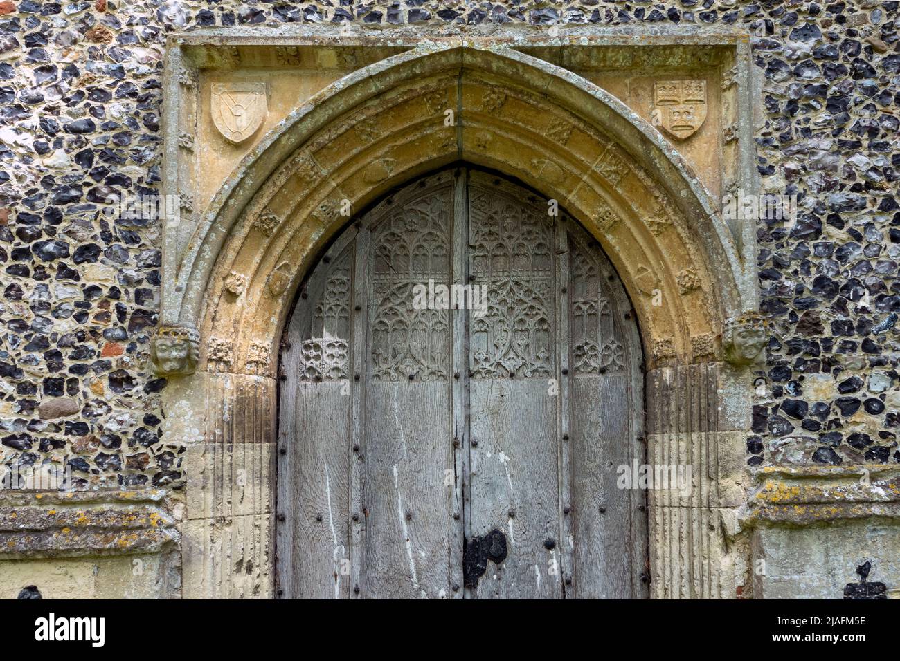 Finely carved wooden door set in decorative stone archway in a flushwork flint wall, All Saints Church, Brandeston, Suffolk Stock Photo