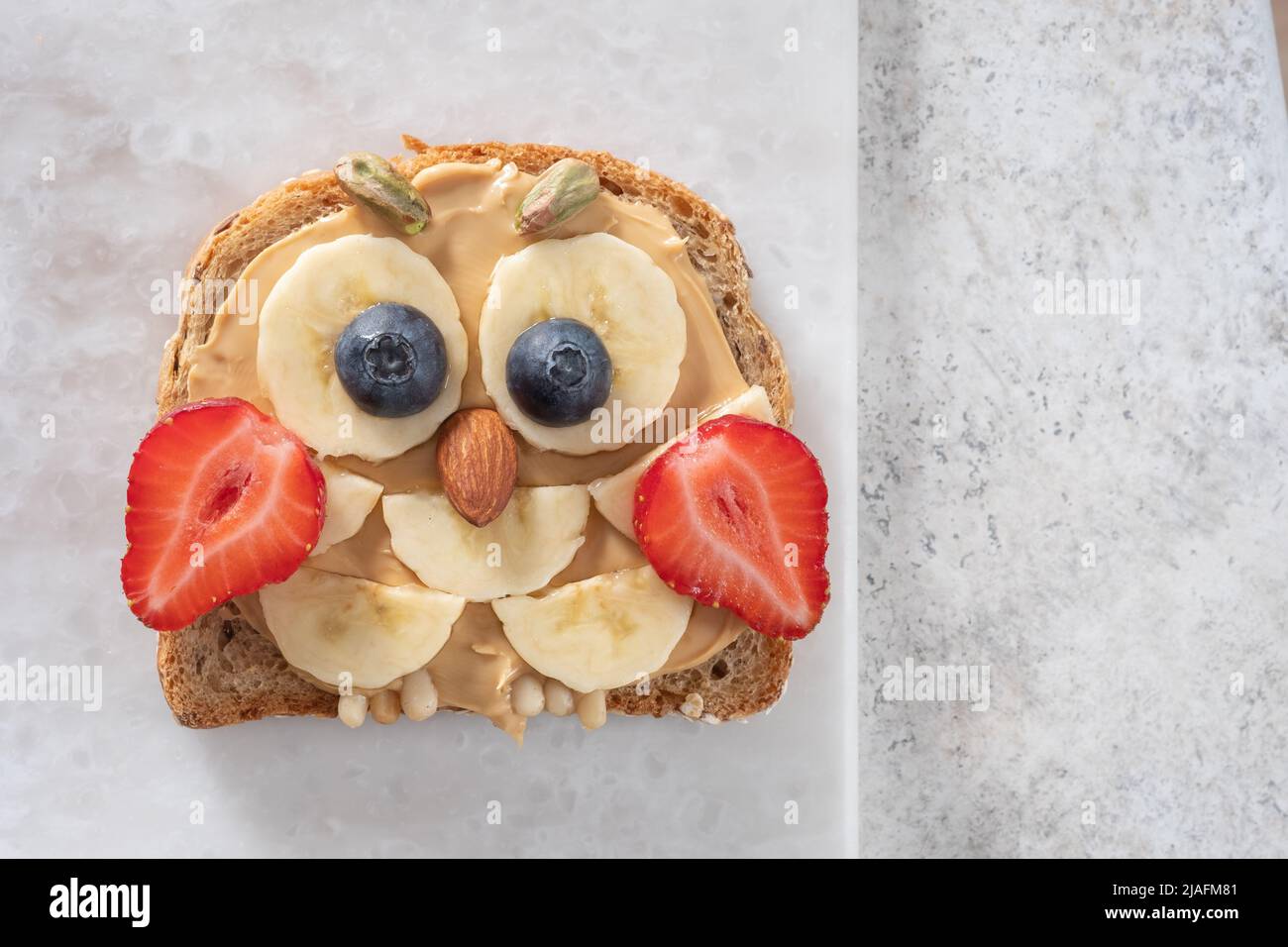 Kids breakfast or lunch or snack toast with peanut butter spread, banana, strawberry and blueberry shaped as cute owl. Stock Photo