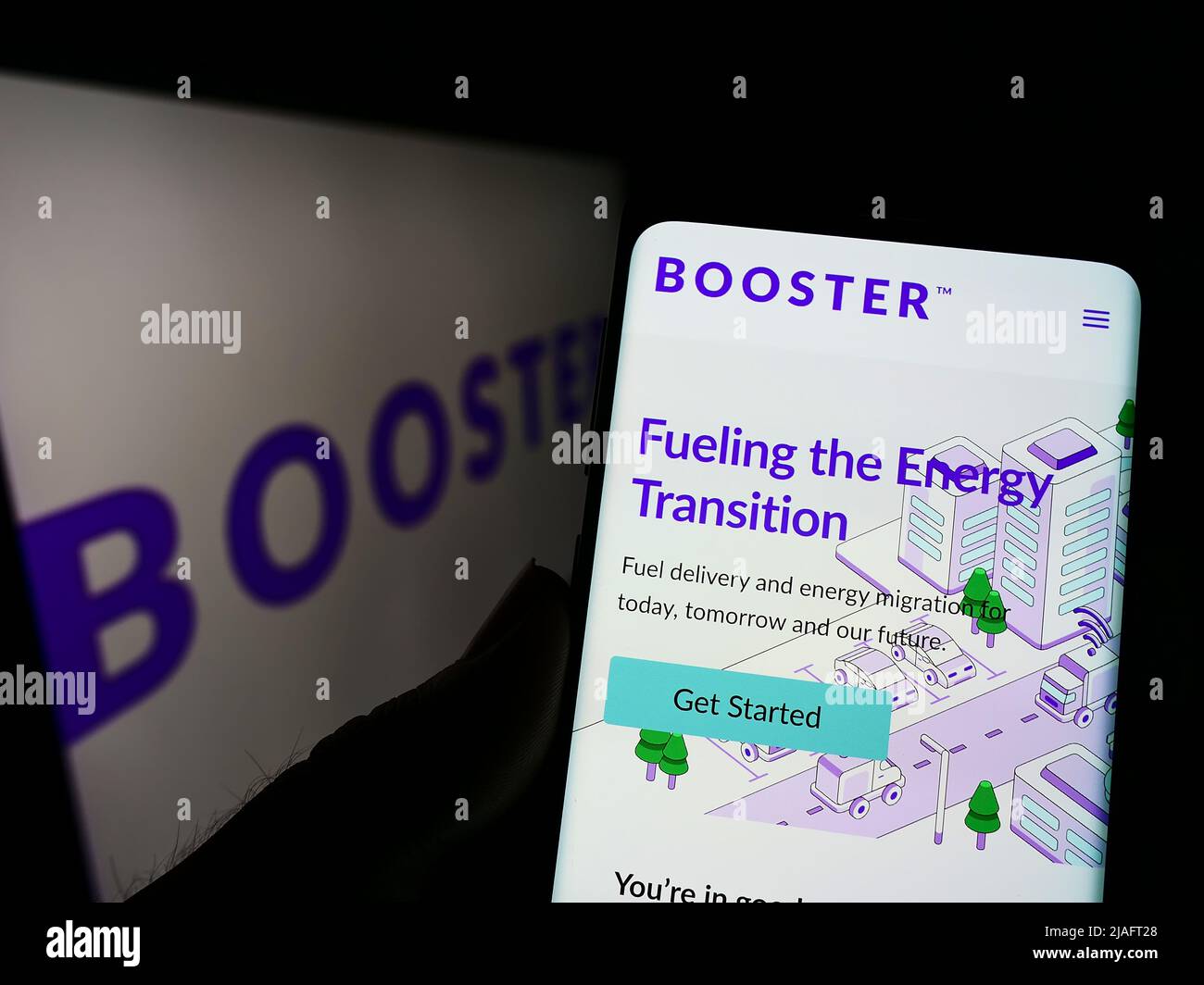 Person holding cellphone with webpage of US energy delivery company Booster Fuels Inc. on screen with logo. Focus on center of phone display. Stock Photo