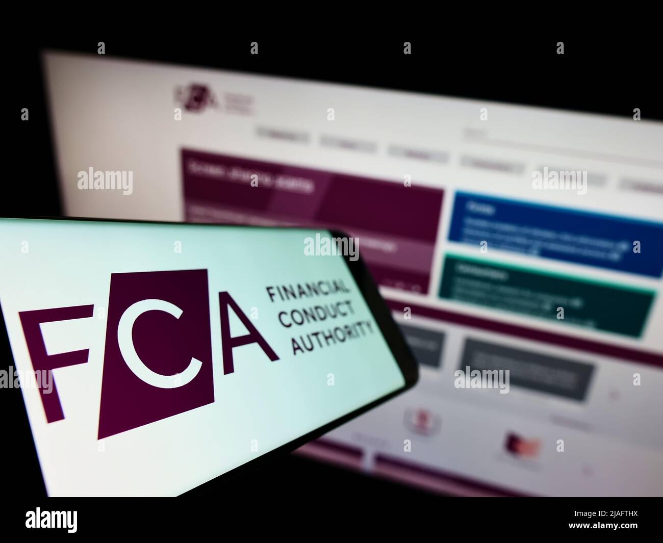 Smartphone with logo of British regulatory body Financial Conduct Authority (FCA) on screen in front of website. Focus on left of phone display. Stock Photo