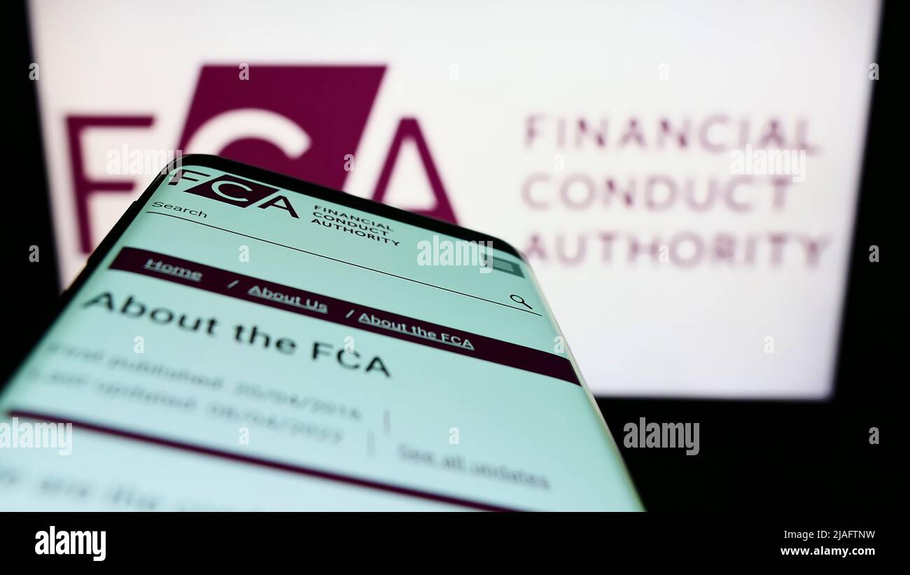 Mobile phone with website of British Financial Conduct Authority (FCA) on screen in front of logo. Focus on top-left of phone display. Stock Photo