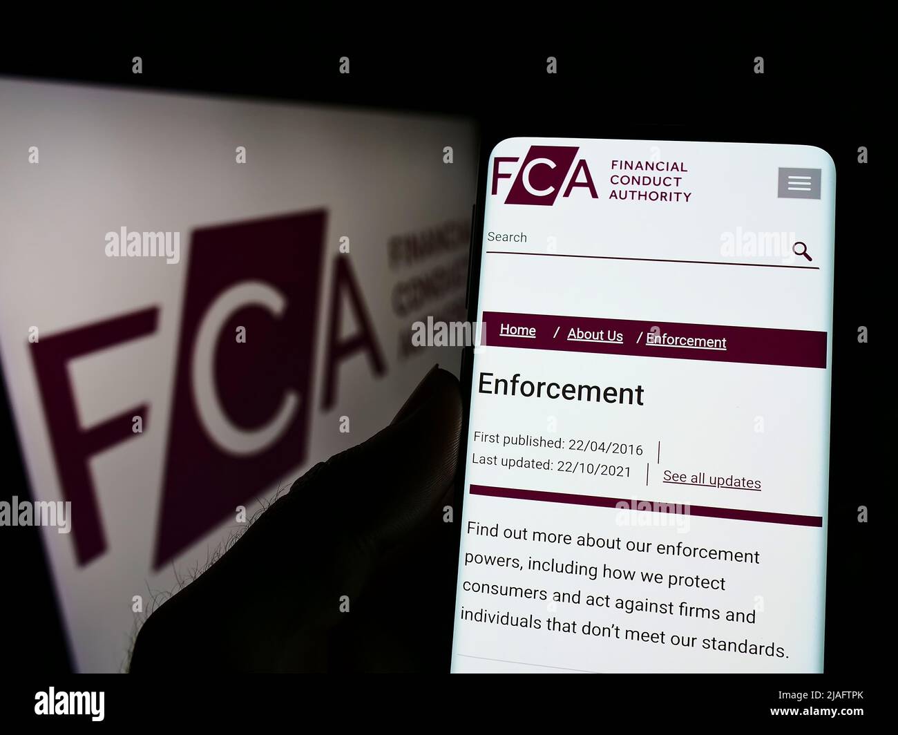 Person holding cellphone with webpage of British Financial Conduct Authority (FCA) on screen in front of logo. Focus on center of phone display. Stock Photo
