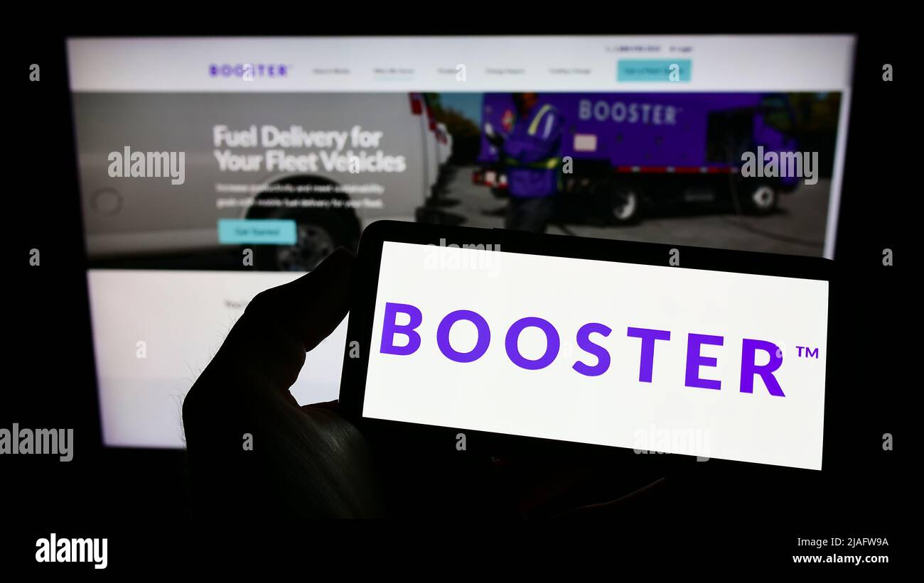 Person holding mobile phone with logo of American energy delivery company Booster Fuels Inc. on screen in front of webpage. Focus on phone display. Stock Photo