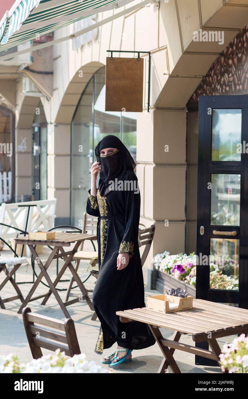 A Muslim woman in national dress walks past empty tables cafe. Stock Photo