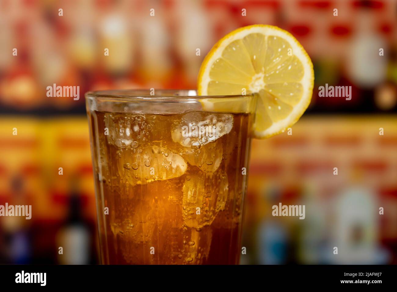 Glass with sparkling cola, ice and lemon on a wooden counter in front of a bar Stock Photo