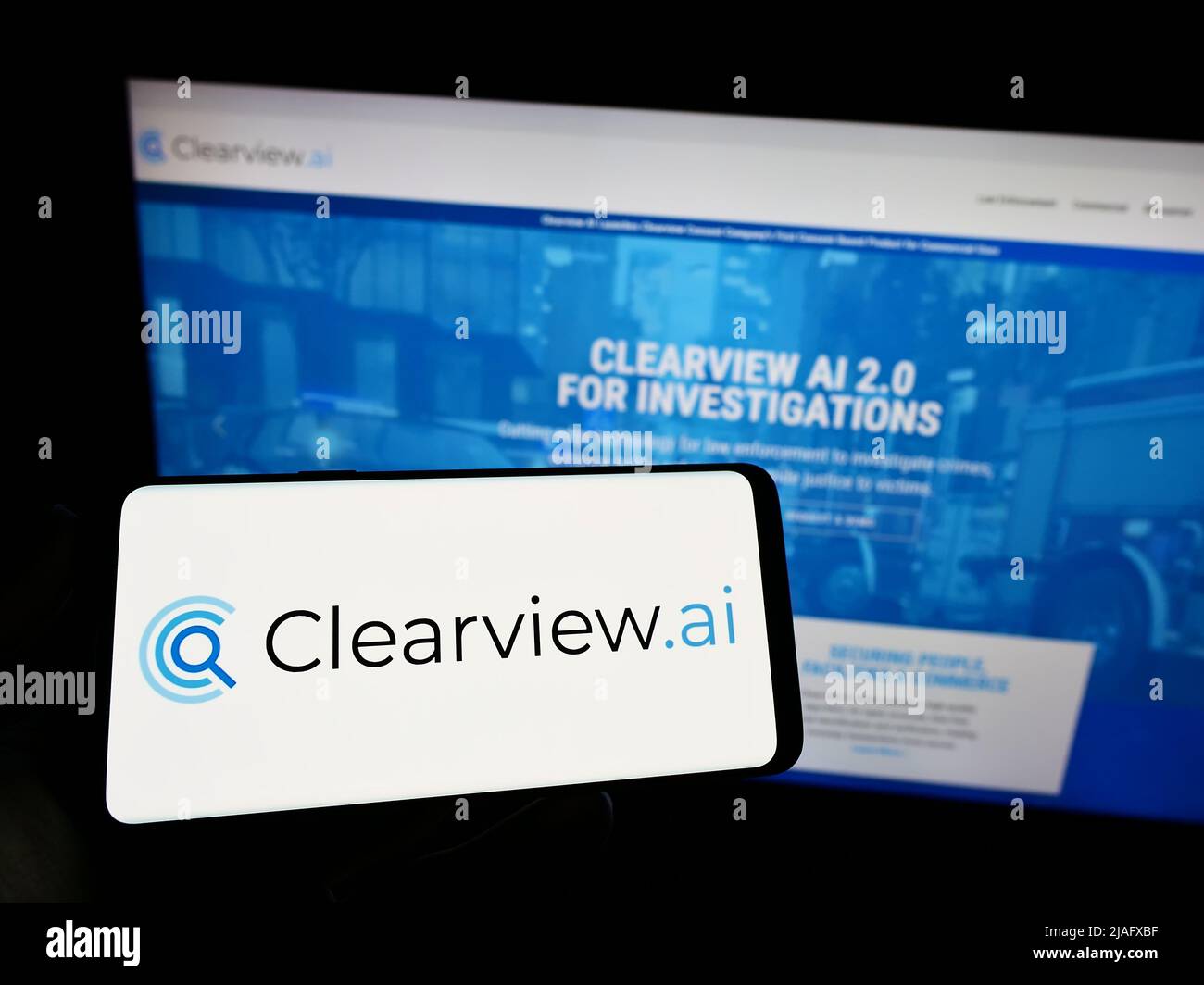 Person holding mobile phone with logo of facial recognition company Clearview AI Inc. on screen in front of web page. Focus on phone display. Stock Photo