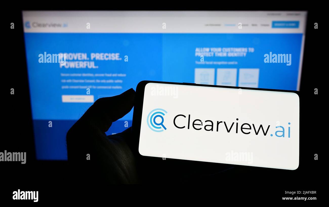 Person holding cellphone with logo of facial recognition company Clearview AI Inc. on screen in front of business webpage. Focus on phone display. Stock Photo