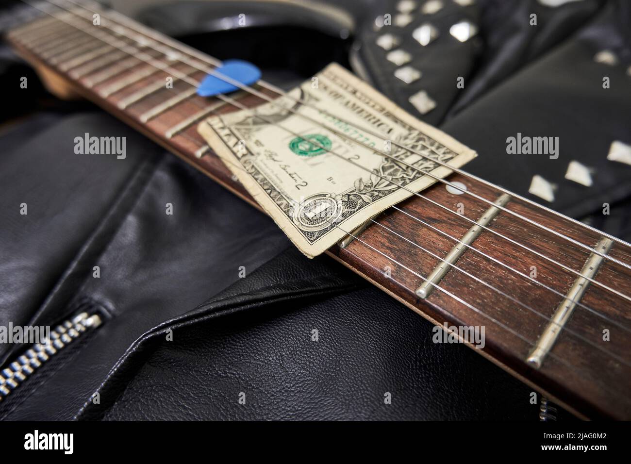 One dollar bill, guitar neck, guitar pick, and leather jacket