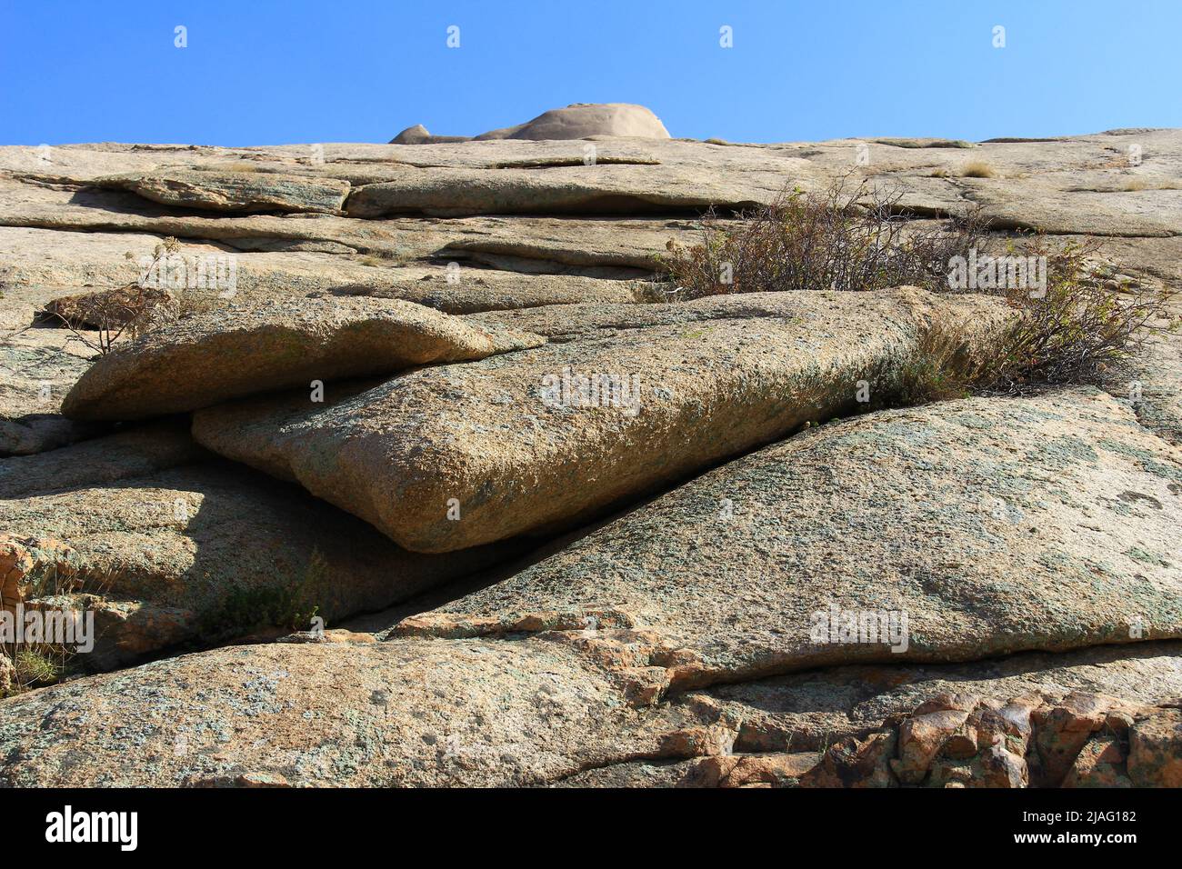 Volcanic layered flat rocks and stones of various shapes with dry bushes in the Bektau-Ata tract against the sky in summer Stock Photo
