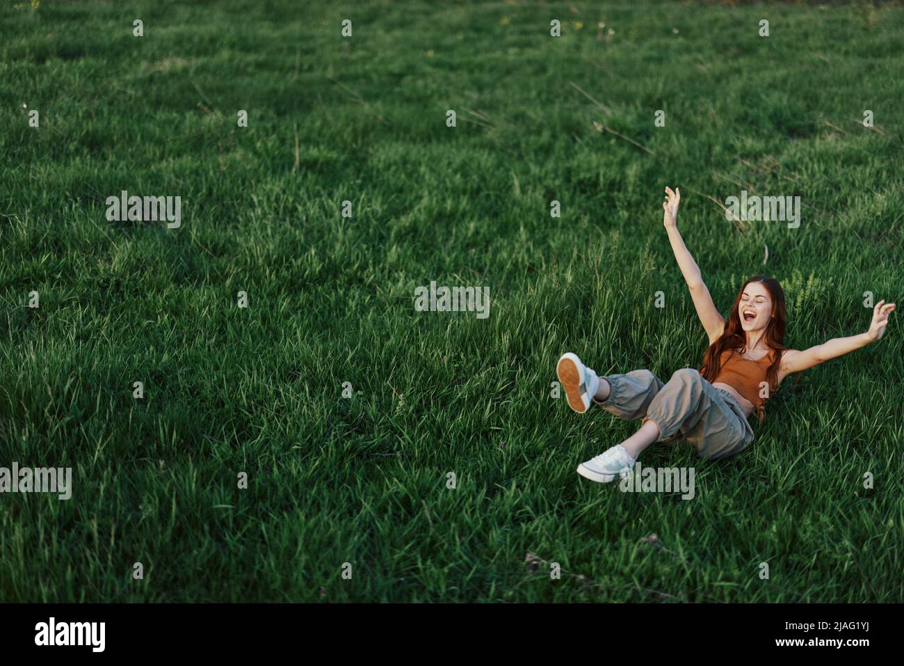 A Young Woman Playing Games In The Park On The Green Grass Spreading   A Young Woman Playing Games In The Park On The Green Grass Spreading Her Arms And Legs In Different Directions Falling And Smiling In The Summer 2JAG1YJ 