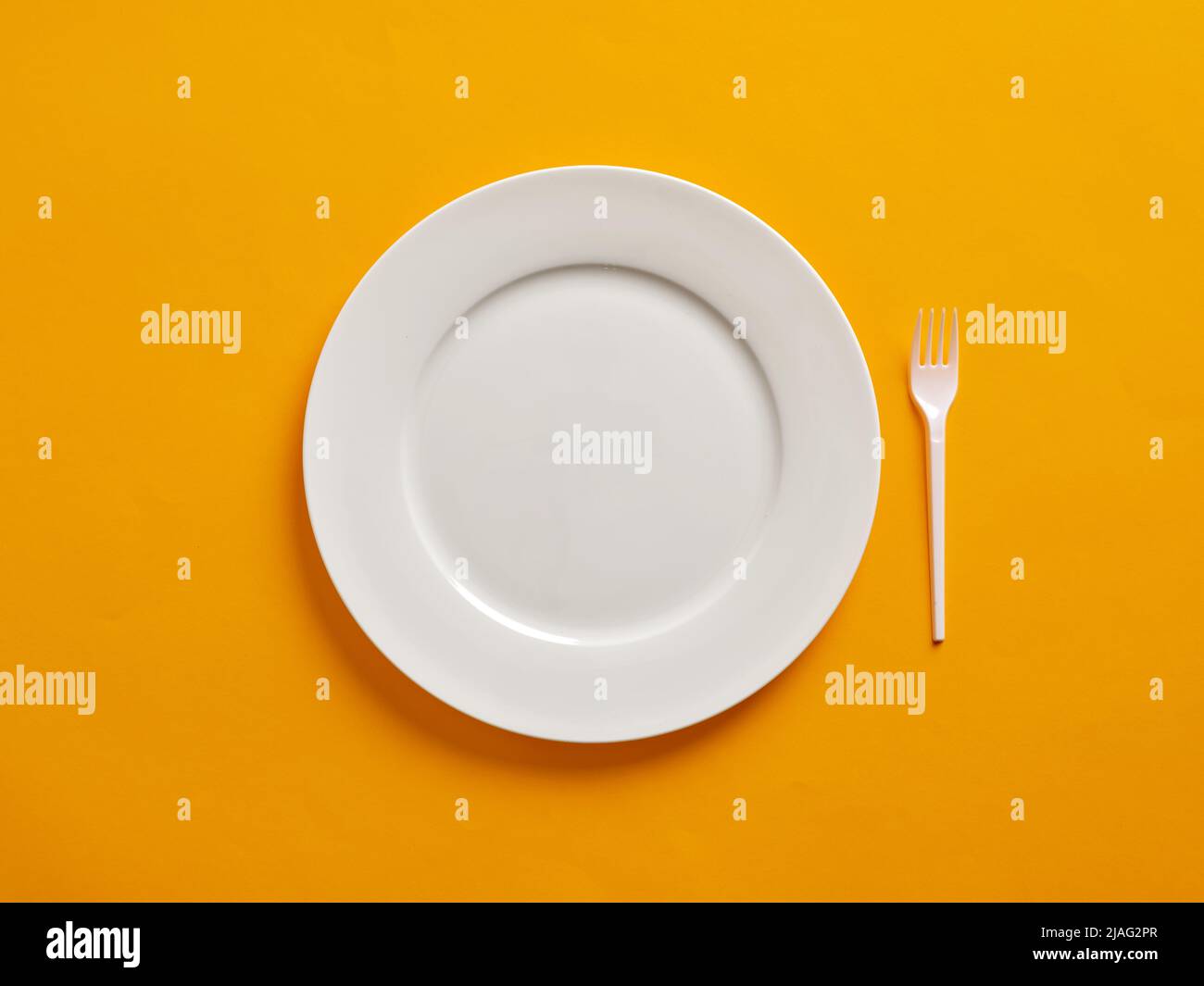 Empty or blank white plate with plastic fork on yellow background. Stock Photo