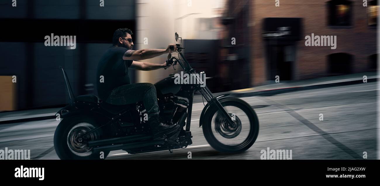 Serious brutal biker rushes on a motorcycle through the evening metropolis. Unfocus effect. Concept of fashion, style and hobby, aspiration Stock Photo