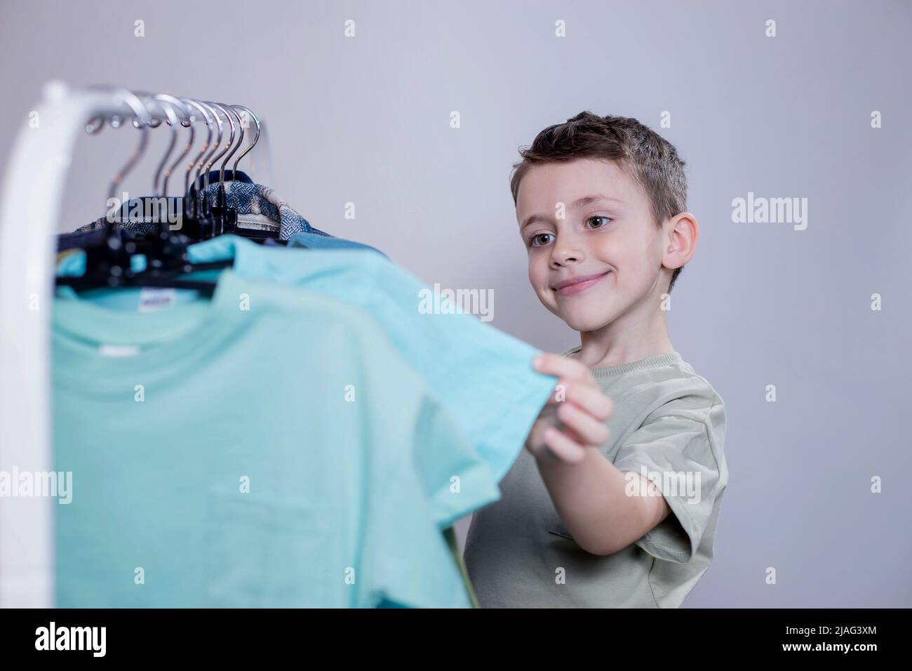 Boy preschooler standing by the hangers, racks up clothes, and chooses ...