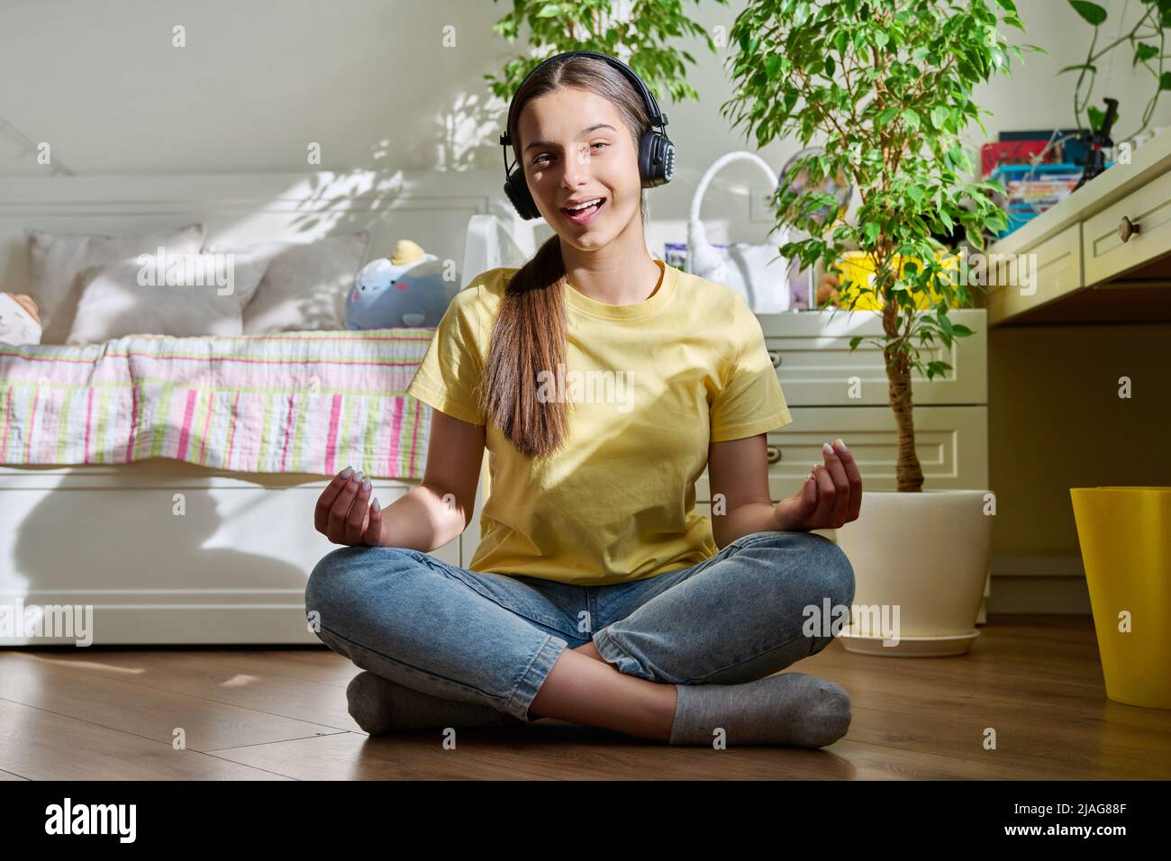 Teenage girl in headphones relaxing sitting in lotus position at home ...