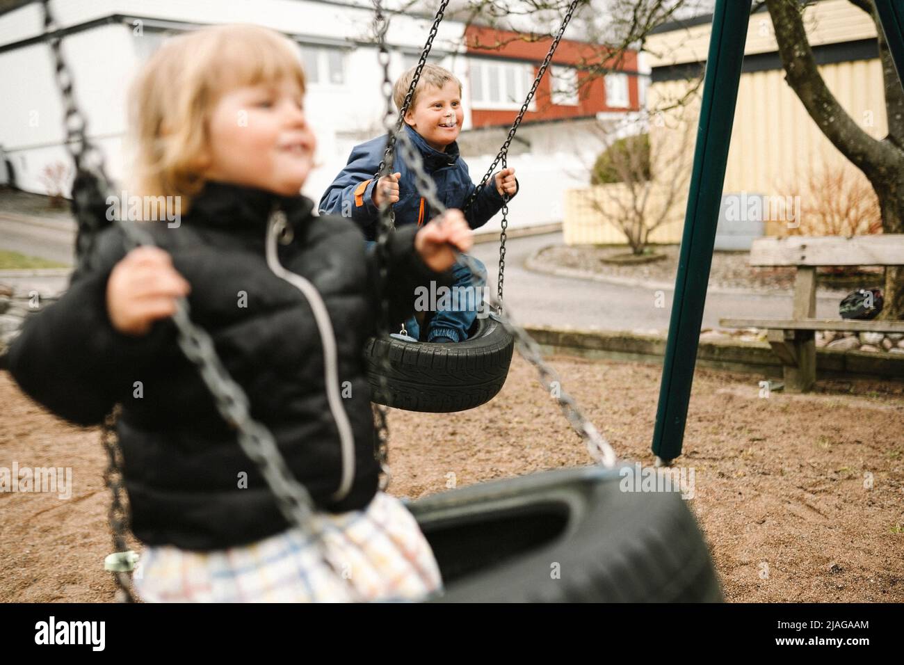 Playful brother and sister having fun on tire swing at park Stock Photo