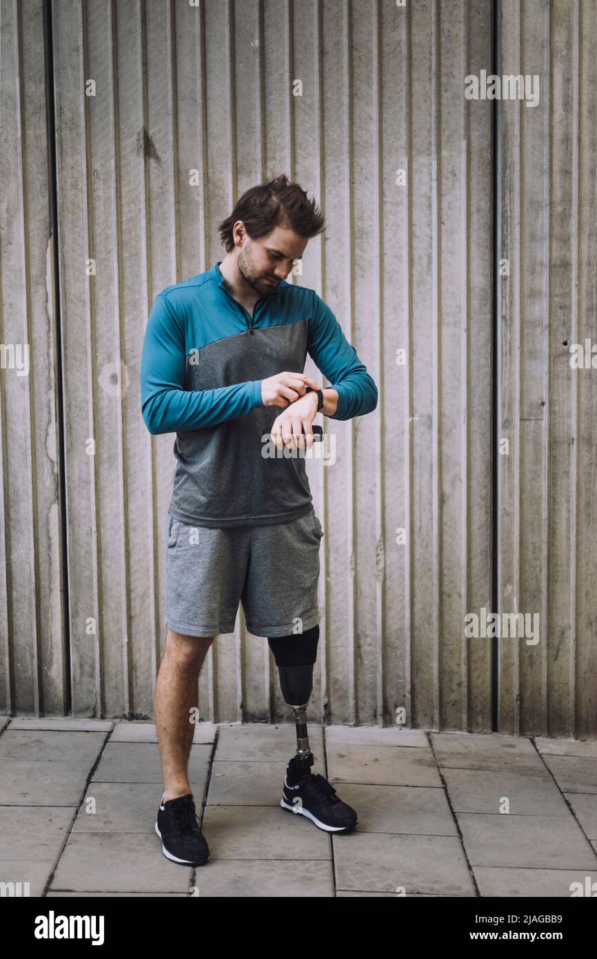 Young man with disability checking time while standing on footpath against wall Stock Photo