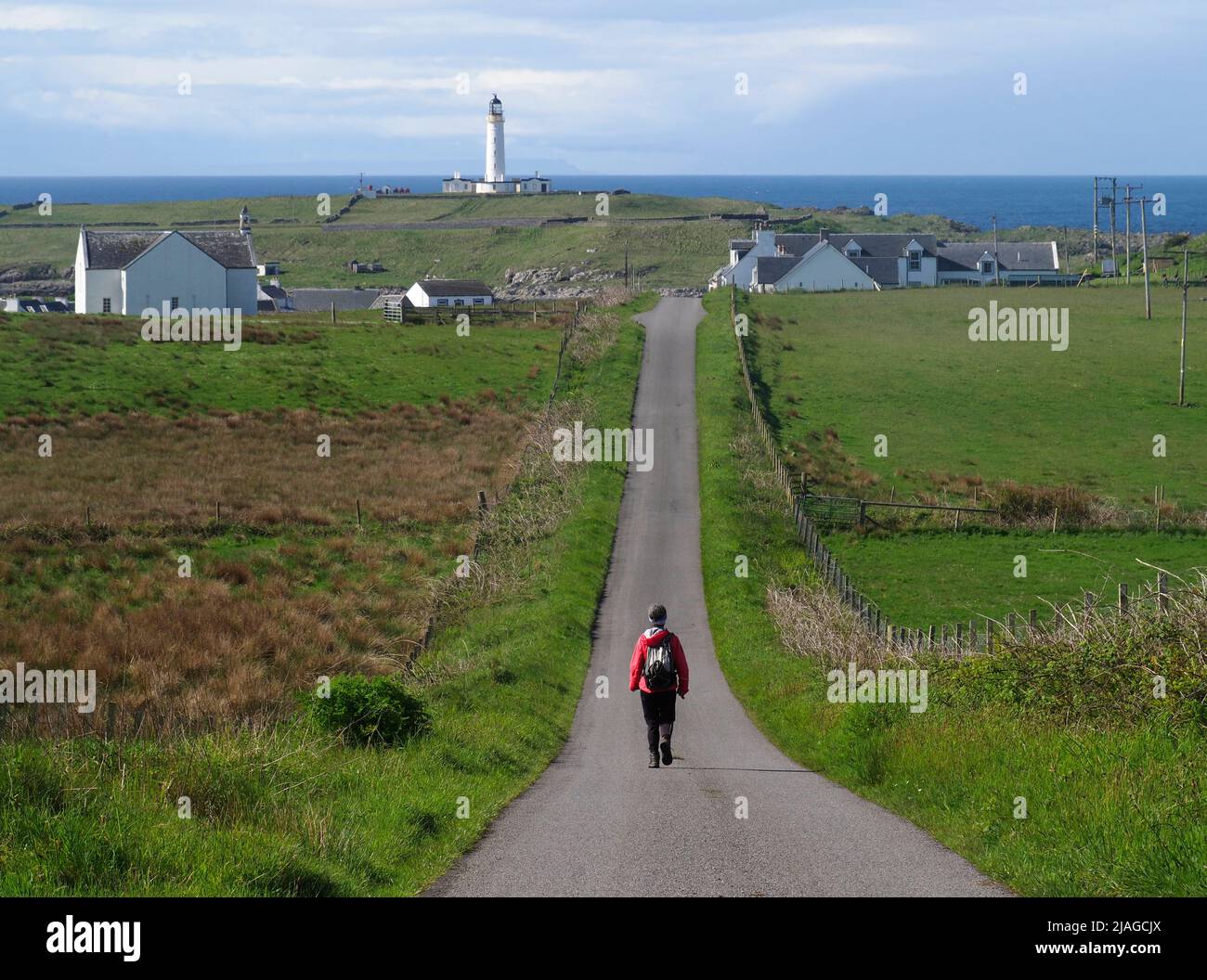 Walker on road to Portnhaven and Orsay lighthouse, Rinns of Islay Stock Photo