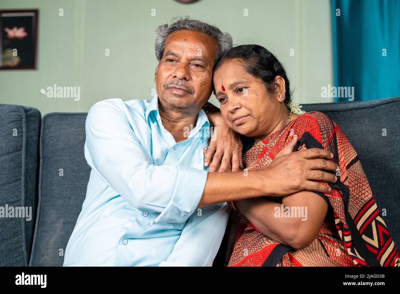 Senior man consoles by embracing his thouhgtful wife at home while on sitting sofa - concept of family, emotional love and support Stock Photo