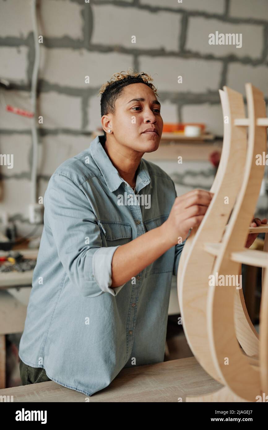 Vertical portrait of modern female carpenter designing wooden furniture piece in workshop interior Stock Photo