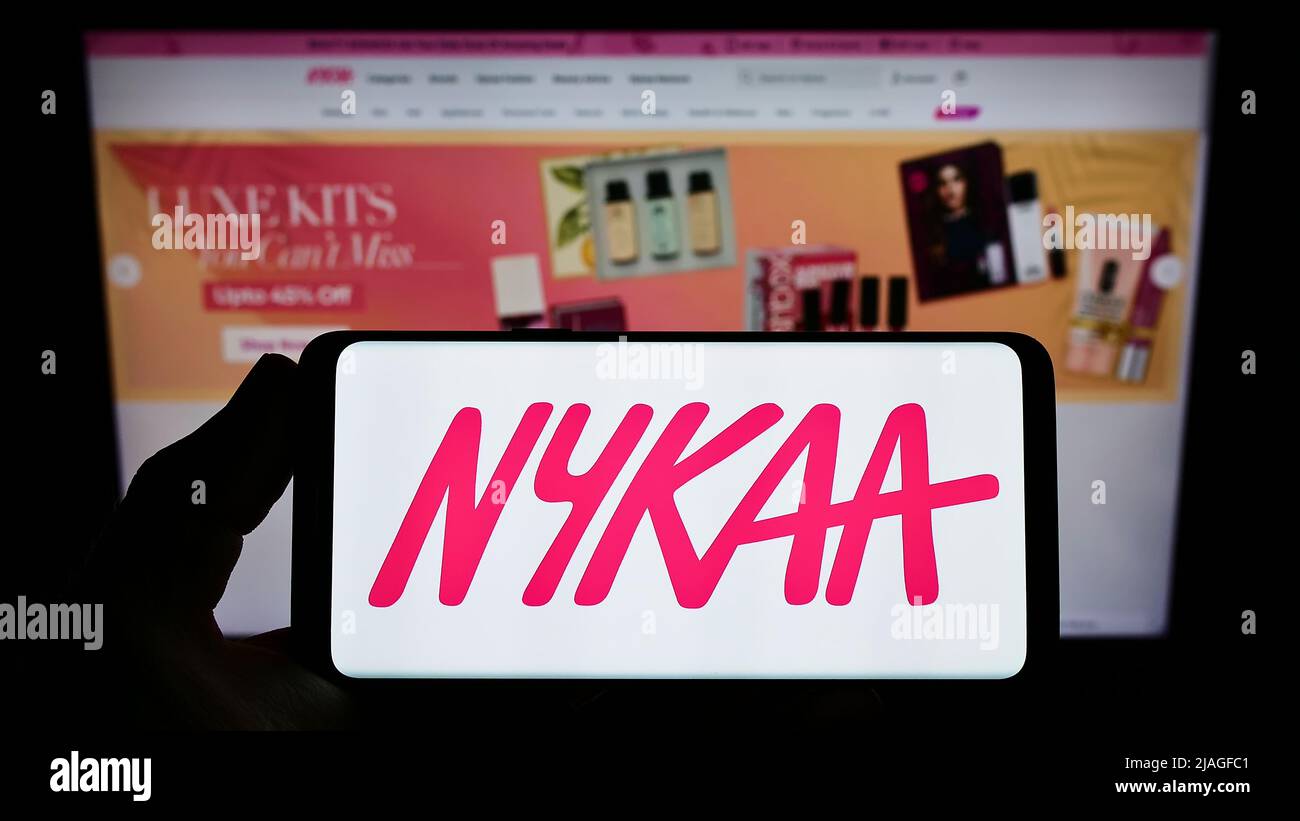 Person holding smartphone with logo of e-commerce company Nykaa E-Retail Pvt. Ltd. on screen in front of website. Focus on phone display. Stock Photo