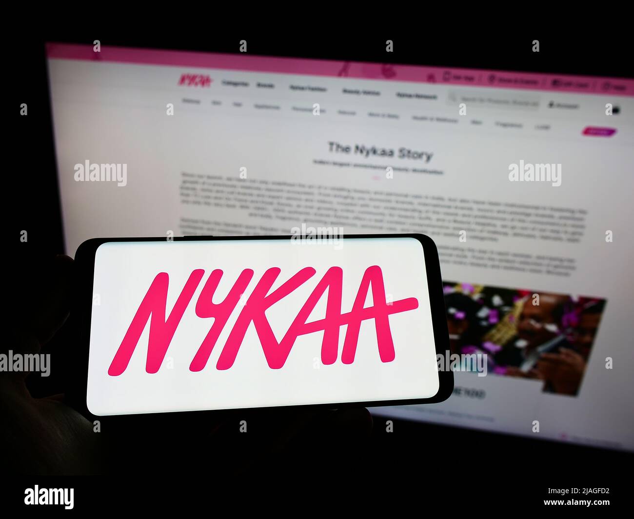 Person holding mobile phone with logo of e-commerce company Nykaa E-Retail Pvt. Ltd. on screen in front of web page. Focus on phone display. Stock Photo